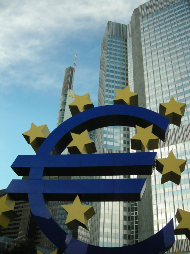 Euro-Zeichen vor dem Hauptquartier der Europäischen Zentralbank in Frankfurt, Deutschland, mit Bäumen und einem bewölkten Himmel im Hintergrund.