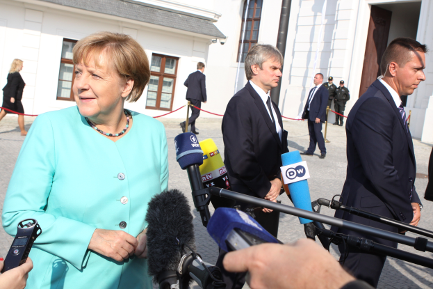 Bundeskanzlerin Angela Merkel bei einer Pressekonferenz im Kanzleramt in Berlin, umgeben von Menschen mit Mikrofonen, mit Gebäuden im Hintergrund.