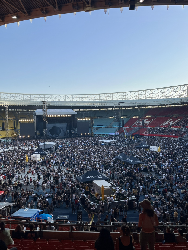 Große Menschenmenge auf Sitzplätzen und Stehplätzen in einem Stadion mit Zelten, Gittern und Flutlicht bei einem Konzert in der O2 Arena in London.