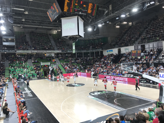 Basketballspiel in einer großen Arena mit Zuschauern, mit den Teams Asvel und Galatasaray, wie auf den Courtside-Boards zu sehen.