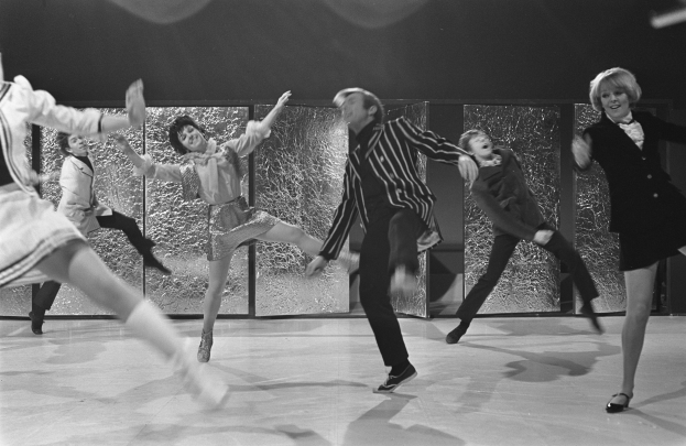 Eine Gruppe von Menschen, die auf einer Bühne tanzen, mit einer Wand im Hintergrund, in einem Schwarz-Weiß-Bild, mit Schuhen.