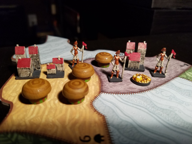 Nahaufnahme eines Spielbretts mit Miniaturen einschließlich Spielzeug, Gebäuden und anderen Gegenständen auf einem dunklen Hintergrund.