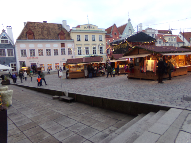 Ein gesch├Ąftiges Weihnachtsmarkt in Tallinn, Estland mit Menschen um dekorierte St├Ąnde, festliche Geb├Ąude und Topfpflanzen.