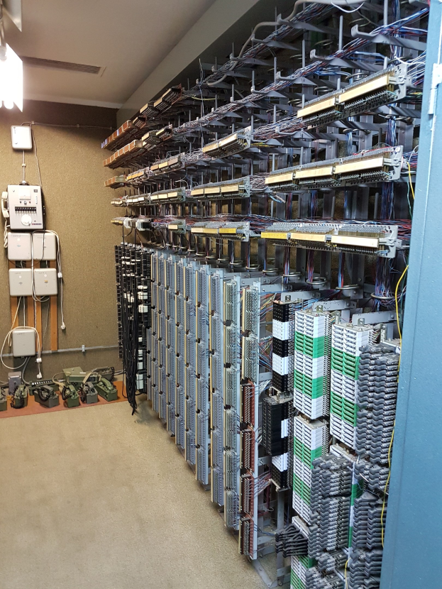 Großer Raum voller Numerous Drähte, elektronische Geräte und Server auf dem Boden, mit einer Wand auf der linken Seite, was auf eine Rechenzentrumseinrichtung hindeutet.