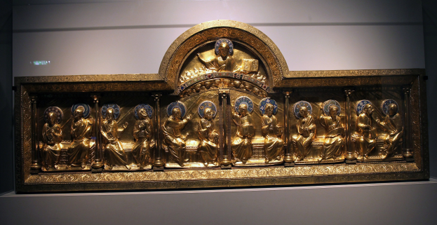 Ein prunkvoller goldener Rahmen in einem Museum ausgestellt, verziert mit Skulpturen, mit einer Wand im Hintergrund.