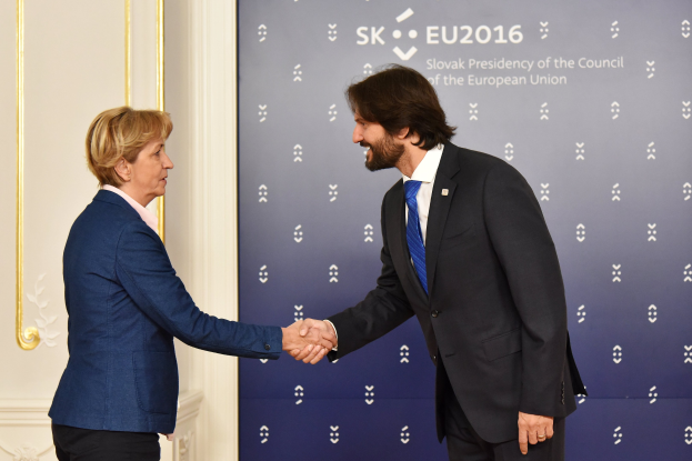 Bundeskanzlerin Angela Merkel und Bundeskanzler Joachim Gauck schütteln sich l├Ąchelnd vor einer Wand mit einem "EU-Gipfel"-Banner und einer Tür.