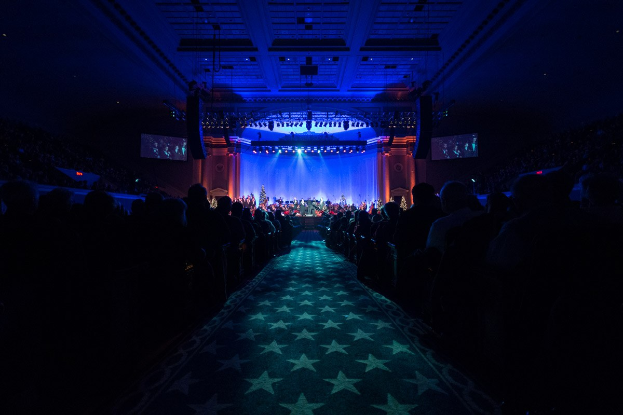 Ein großer Saal mit Sitzplätzen, eine Bühne mit Musikern und Überkopfbeleuchtung und -fernseher, was auf einen Konzertsaal während der Nationalen Convention 2019 hinweist.