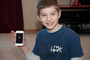 Ein Junge hält ein Handy vor einer Wand.