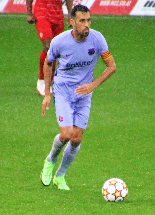 Fußballspieler in Sportbekleidung und Fußballschuhen auf dem Feld mit einer Tafel im Hintergrund.