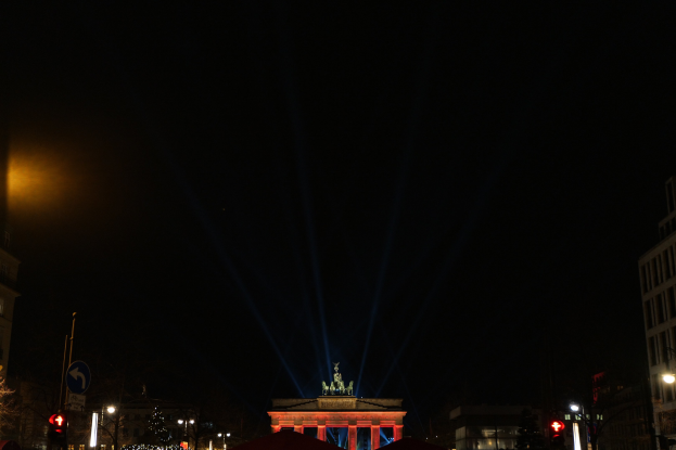 Das Brandenburger Tor nachts, beleuchtet von Straßenlaternen, mit umliegenden Gebäuden, Bäumen, Pfählen, Verkehrsampeln, Schildern und Zelten gegen einen dunklen Himmel.