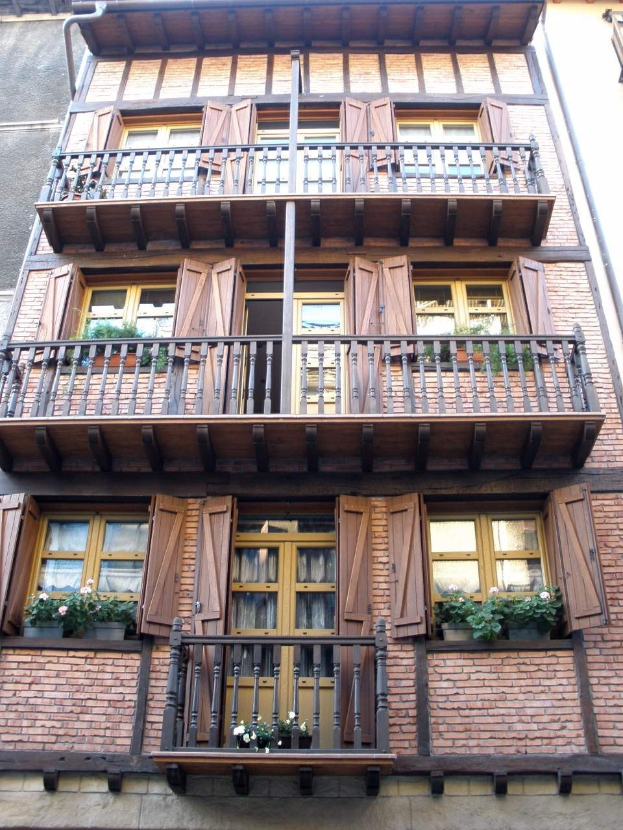 Ein mehrstöckiges Gebäude mit zahlreichen Fenstern, Balkonen, Geländern und Blumenkisten in Straßburg, Frankreich.