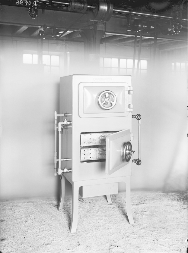 Schwarz-weiß-Foto eines alten Tresors in einem Raum mit einer Wand, Fenstern und Rohren an der Decke.