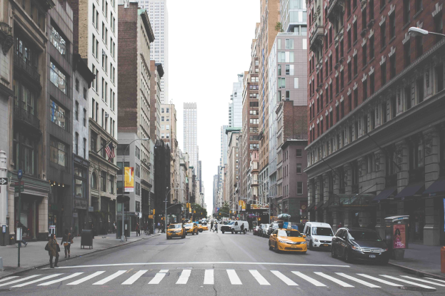 Eine belebte Stadtstraße mit hohen Gebäuden, Fahrzeugen, Fußgängern, Laternenpfählen und großen Werbetafeln mit den Top-Attraktionen in New York City.