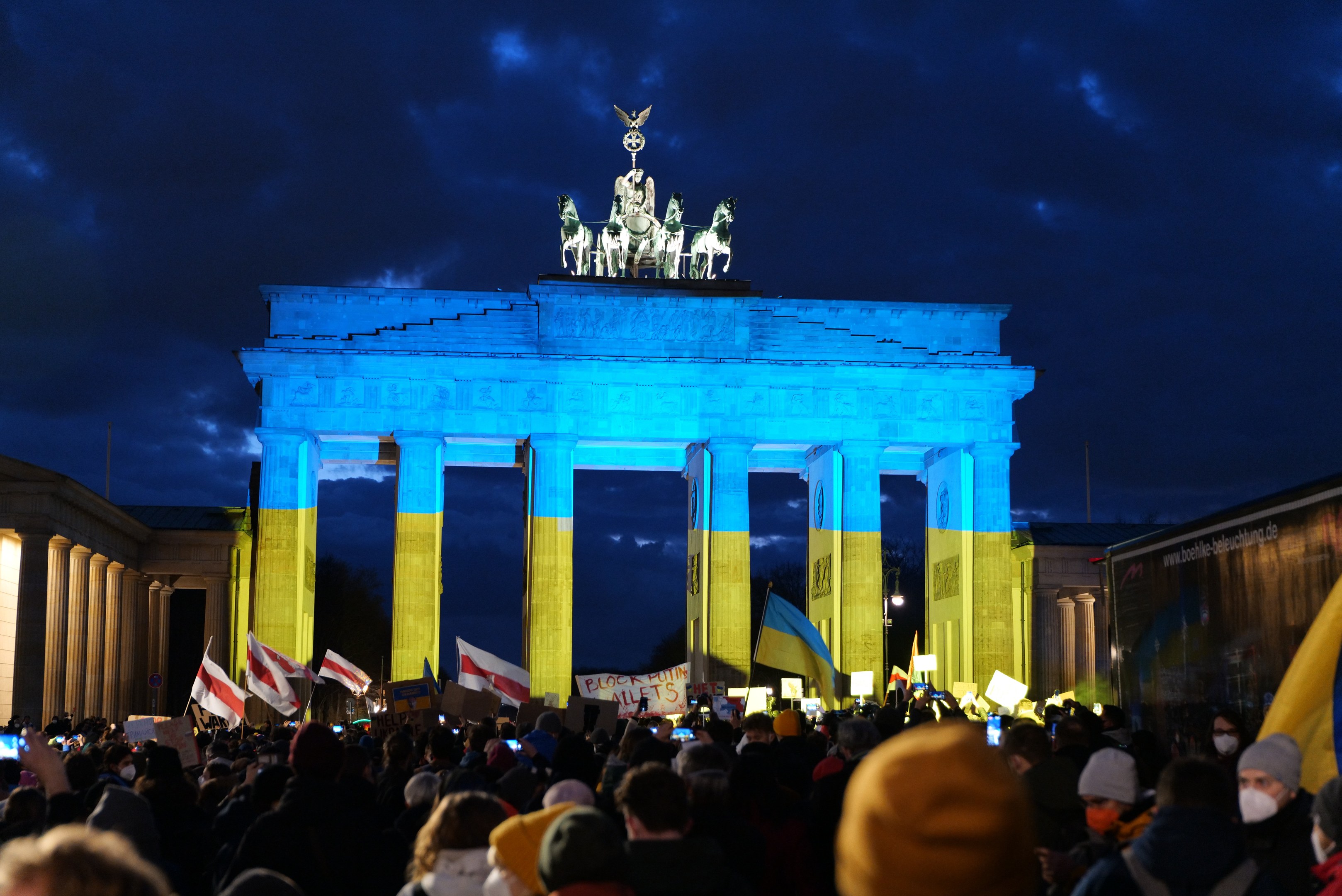 Eine Menschenmenge mit Fahnen und Transparenten steht vor dem Brandenburger Tor in Berlin, Deutschland, mit einer Fahne auf der rechten Seite des Bildes.