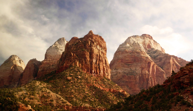 Eine malerische Aussicht auf den Zion-Nationalpark in Utah mit majestätischen Bergen, grünen Bäumen, steinigem Gelände und einem Himmel mit weißen, flauschigen Wolken.