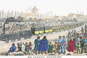 Eine Gruppe von Menschen steht um einen Zug auf einem Gleis, einige sind im Zug und andere außerhalb, in der Nähe von Gebäuden und Bäumen, mit dem Text "Ludwigs-Eisenbahn, die erste Bahnstation in Deutschland" unten.