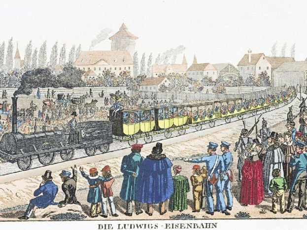 Eine Gruppe von Menschen steht um einen Zug auf einem Gleis, einige sind im Zug und andere außerhalb, in der Nähe von Gebäuden und Bäumen, mit dem Text "Ludwigs-Eisenbahn, die erste Bahnstation in Deutschland" unten.
