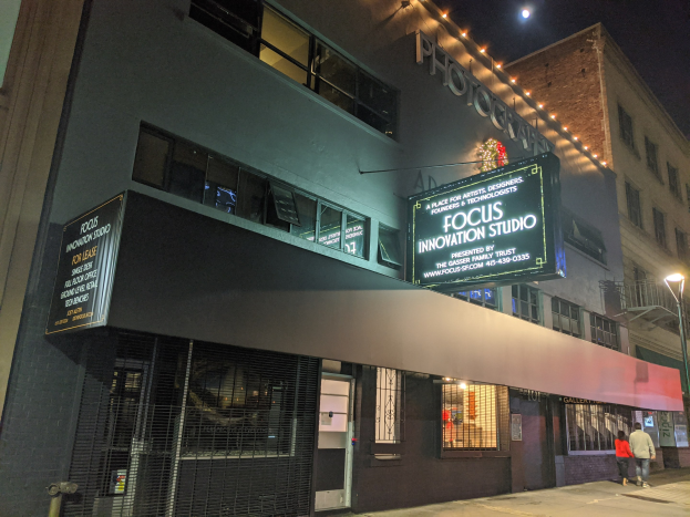Außensicht des Focus Innovation Studios in New York City bei Nacht, mit beleuchteten Gebäuden, Menschen auf dem Gehweg und sichtbarem Himmel im Hintergrund.