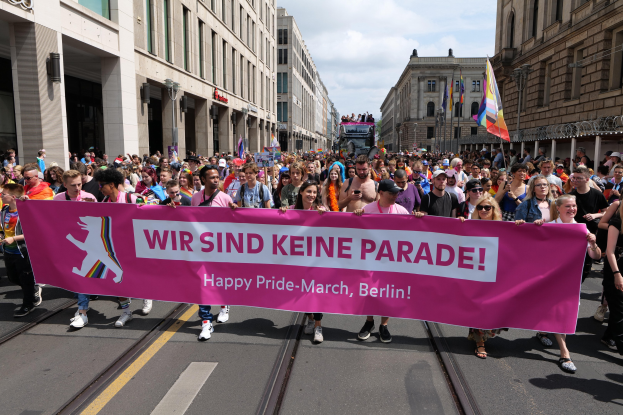 Eine Gruppe von Menschen marschiert eine Berliner Straße entlang und hält ein pinkes Banner mit der Aufschrift "Happy Pride March".