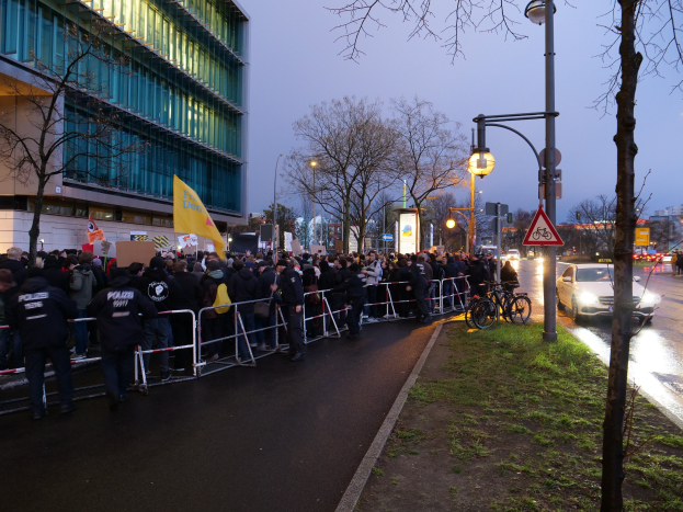Große Menschenmenge vor einem Gebäude in Berlin mit Protestplakaten, Barrikaden und Fahrrädern im Vordergrund.