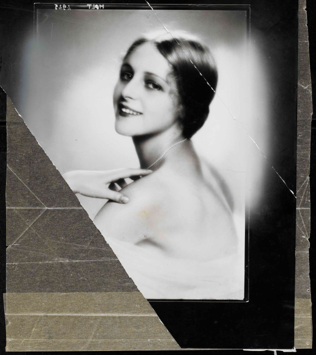 Schwarzes und weißes Foto einer Frau in einem Kleid im Stil der 1920er Jahre mit einem ordentlichen Dutt, die warm in die Kamera lächelt.