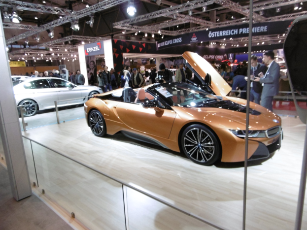 Ein elegantes schwarzes BMW i8 Roadster mit Chromakzenten auf der Frankfurt Motor Show umgeben von formell gekleideten Gästen in einer Atmosphäre der Aufregung.