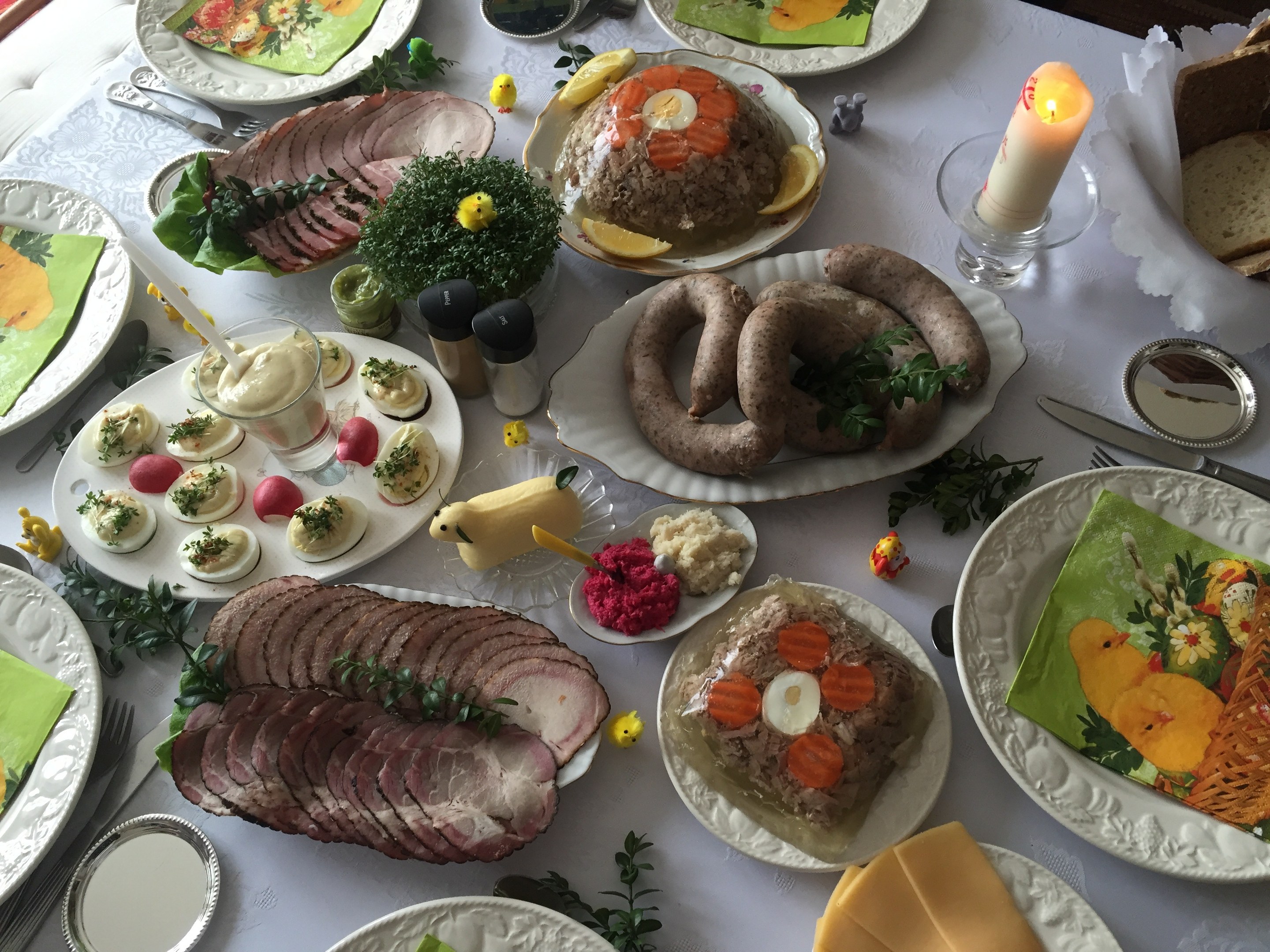 Ein langer Tisch mit verschiedenen Gerichten, Besteck und Kerzen, umgeben von Stühlen, als Zeichen für ein traditionelles deutsches Osteressen.