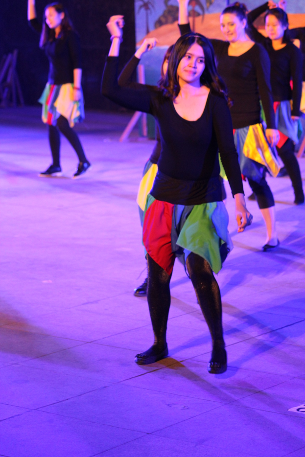 Junge Frauen tanzen auf einer Bühne mit einem Gemälde im Hintergrund, tragen Schuhe während einer Vorstellung.