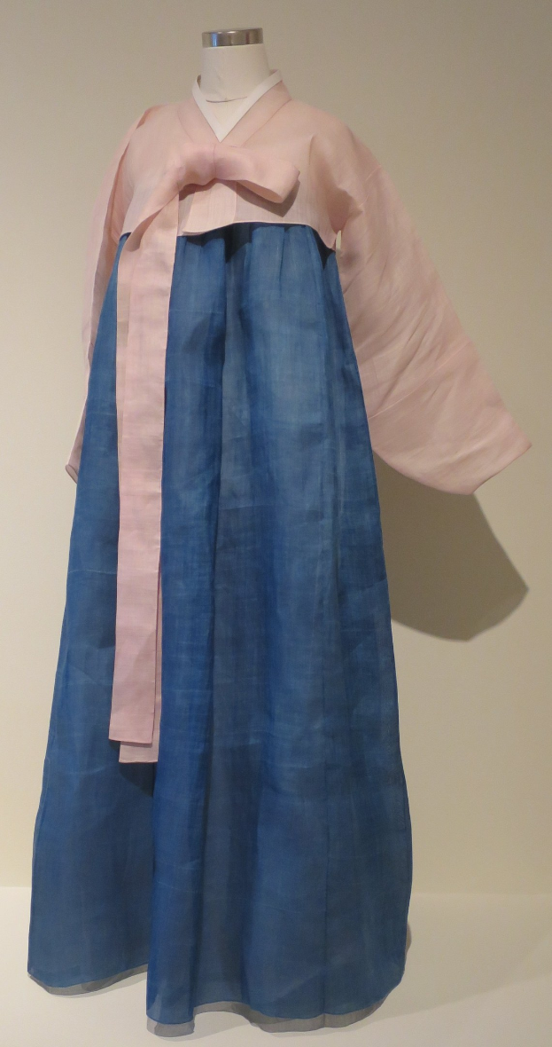 Eine Schaufensterpuppe trägt ein blaues und pinkes hanbok, ein traditionelles koreanisches Kleid, das an einer neutralen Wand in einem Museum ausgestellt ist.