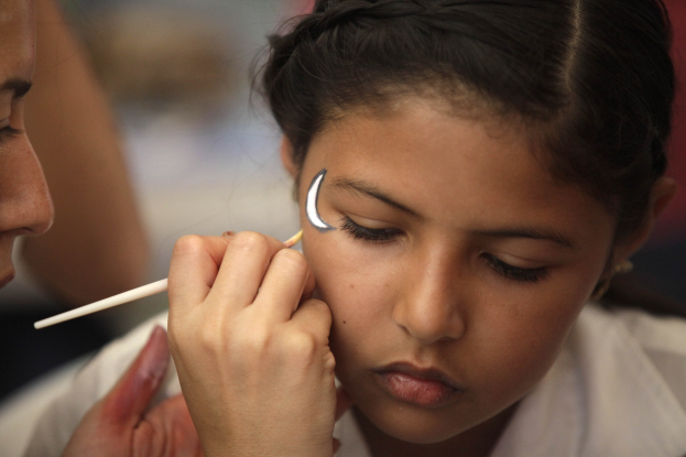 Ein Make-up-Artist trägt Make-up auf das Gesicht eines jungen Mädchens auf, wobei beide klar gegen einen unscharfen Hintergrund abheben.