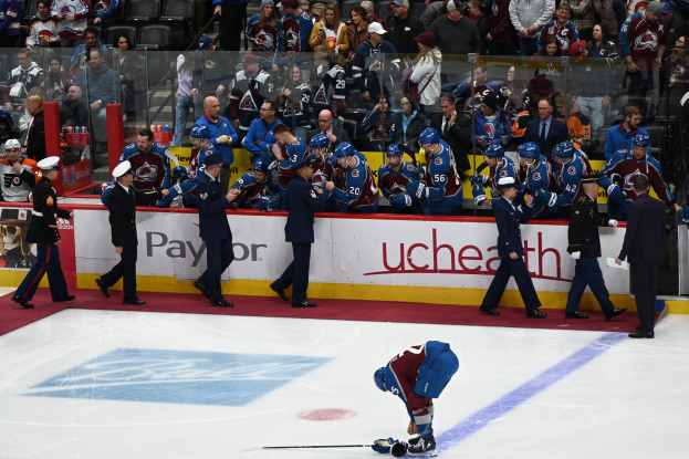 Eishockeyspieler auf dem Eis umgeben von Teamkollegen und Gegnern während eines Spiels, mit Zuschauern im Hintergrund und einer Anzeigetafel, die "Colorado Avalanche vs San Jose Sharks - 3/24/15 NHL Pick, Odds, and Prediction" anzeigt.