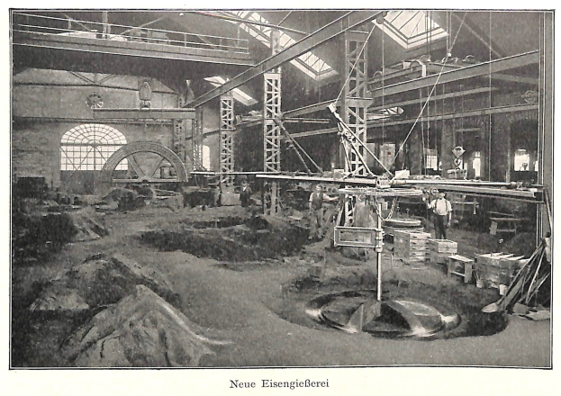 Schwarzes und weißes Foto einer Fabrikhalle mit Arbeitern, die Maschinen bedienen, Metallstangen und -rohre sowie die Beschriftung 'Neue Eisenglebeerei, die erste Fabrik Deutschlands' am unteren Rand.