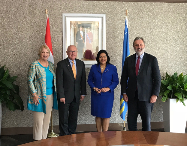 Eine Gruppe von Menschen, die um einen Tisch mit Papieren stehen und lächeln, umgeben von Fahnen, Topfpflanzen und einem Rahmenfoto an der Wand, was die Unterzeichnung eines US-Kanada-Memorandums angibt.