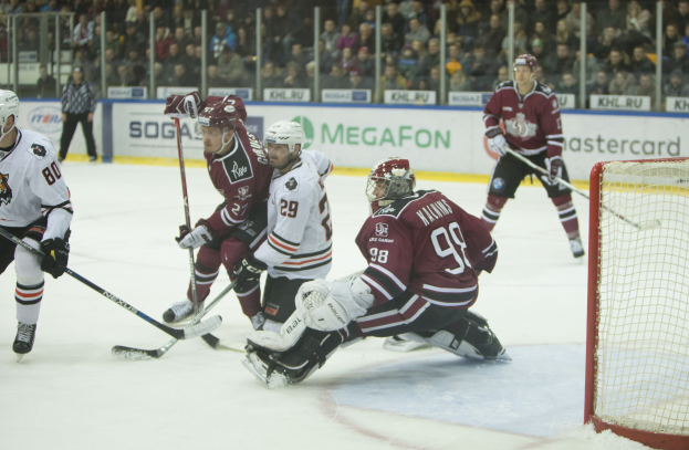 Gruppe von Menschen, die Hockey auf einem Eisstadion spielen, mit Tor auf der rechten Seite, tragen Helme und halten Stöcke, Zuschauer auf Tribüne mit Bannern im Hintergrund.