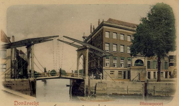 Altes Schwarz-Weiß-Foto einer Brücke im Bau über einen Fluss mit Gebäuden, Bäumen und einem klaren Himmel im Hintergrund und verstreute Bauwerkzeuge und Materialien in der Nähe der Brücke.