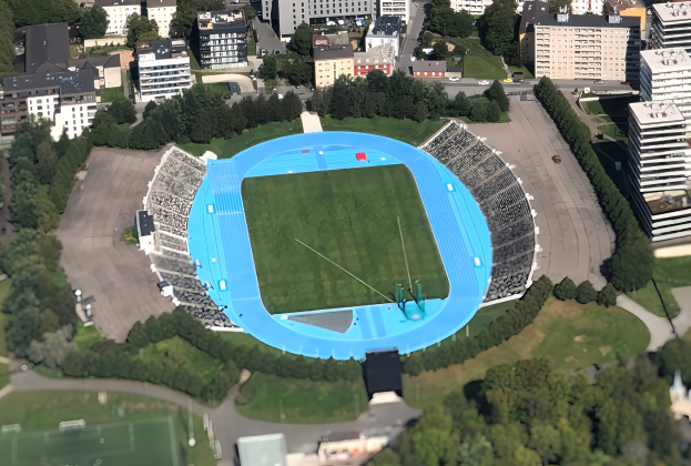 Luftaufnahme des Olympiastadions in München, Deutschland, umgeben von städtischer Infrastruktur wie Gebäuden, Straßen, Fahrzeugen, Bäumen und Gras.