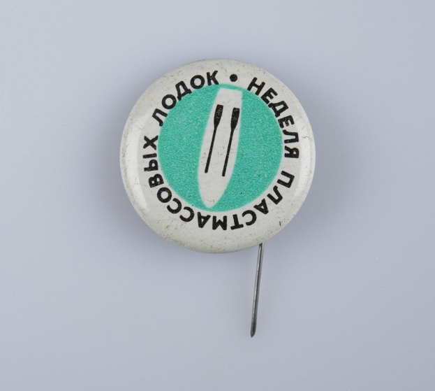 Weißer Ansteckknopf mit grün-weißem Design auf einer weißen Oberfläche, mit Text.