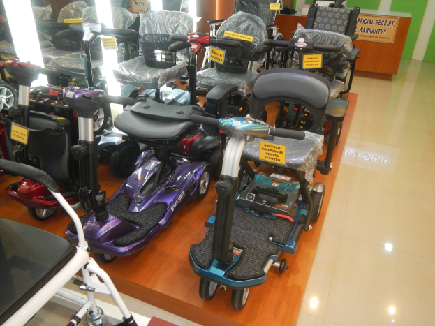 Eine Reihe von E-Scootern in einem Geschäft mit Preisschildern, einem Holztisch mit einer Tafel im Hintergrund und sichtbarem Boden.