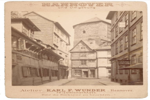 Ein altes Foto einer Straße in Hannover, Deutschland, mit Gebäuden auf beiden Seiten und Text oben und unten im Bild.