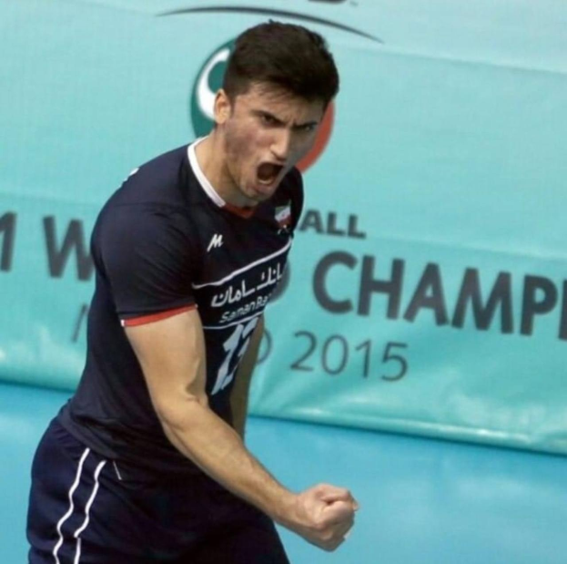 Ein Mann in einem blauen Hemd und schwarzen Shorts spielt Handball mit einem "Kabaddi World Cup 2015"-Plakat im Hintergrund.