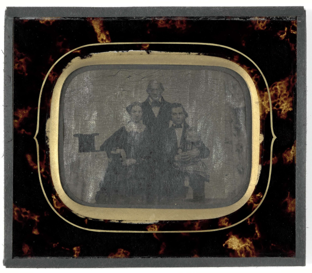 Schwarz-weißes Foto eines Mannes in Anzug und Krawatte und einer Frau in unbekannter Kleidung, die vor einem alten Fernseher stehen, beide mit ernsten Gesichtern.