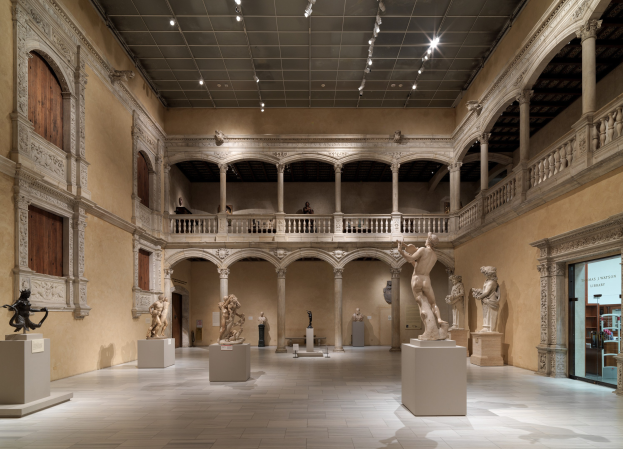 Große Museumsgalerie mit zahlreichen Statuen und Skulpturen auf Sockeln, architektonischen Elementen wie Wänden, Säulen, Geländern und Deckenleuchten sowie einigen Besuchern.