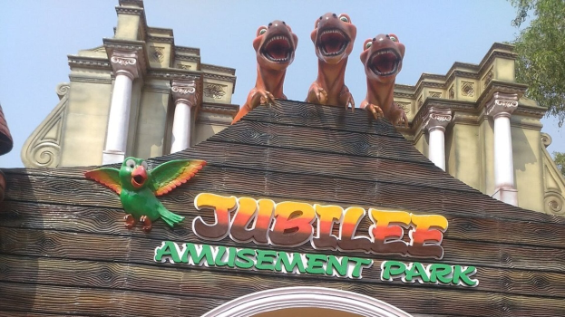 Ein Gebäude mit einem "Jubilee Amusement Park"-Schild, Tierfiguren auf dem Dach, umgeben von Bäumen unter einem klaren blauen Himmel.