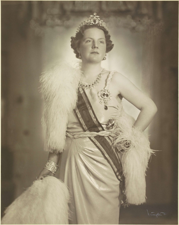 Schwarzes und weißes Foto von Queen Elizabeth II in einem Kleid und einer Krone mit einem unscharfen Hintergrund und Text unten.