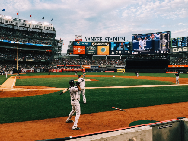 Baseballspiel im Yankee Stadium mit Spielern auf dem Feld und Zuschauern in den Rängen unter einem bewölkten Himmel.