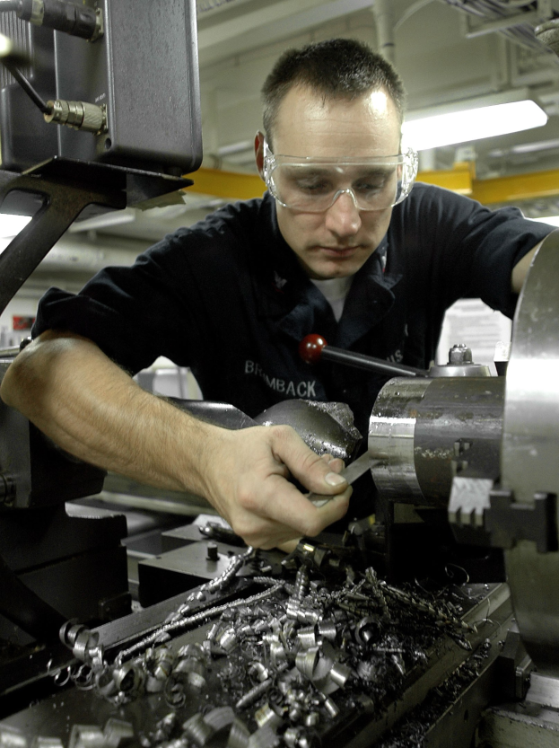 Ein Fräser trägt Schutzbrille und bedient eine Maschine in einer gut beleuchteten Fabrikumgebung.
