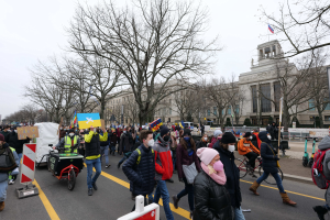 Eine große Gruppe von Menschen marschiert auf einer Straße in einer Stadt, einige halten Schilder und andere fahren Fahrräder, mit Bäumen und einem Gebäude im Hintergrund unter einem klaren blauen Himmel in Washington, D.C. am 21. Januar 2020.