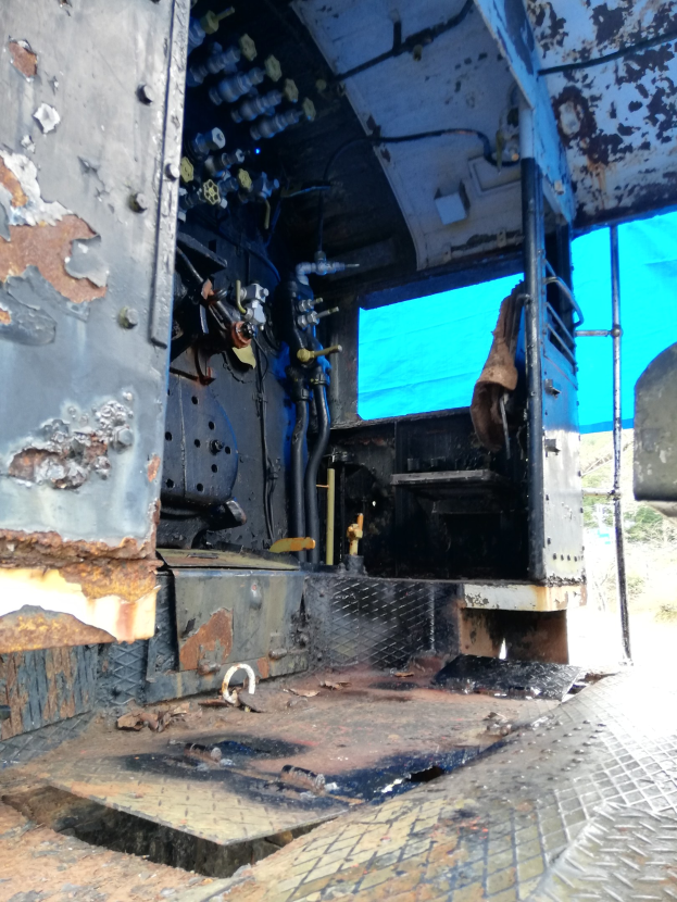 Das Innere eines verrosteten, baufälligen Lkw mit Bäumen und einem klaren blauen Himmel im Hintergrund.