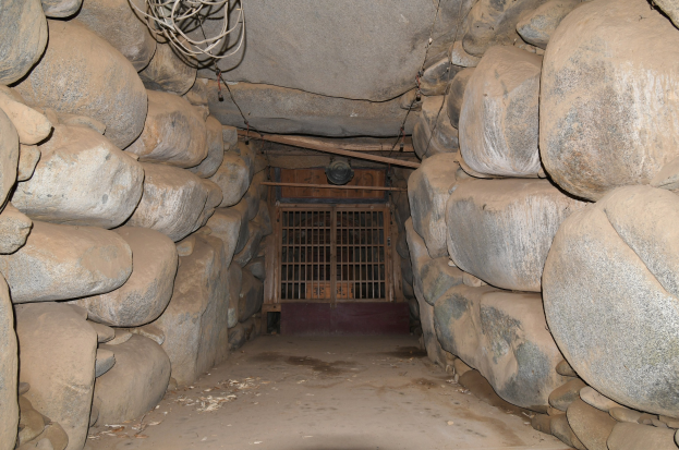 Ein Tunnel voller Steine und ein Metalltor in der Mitte, mit Drähten, die oben entlanglaufen und an einen Minenschacht erinnern.