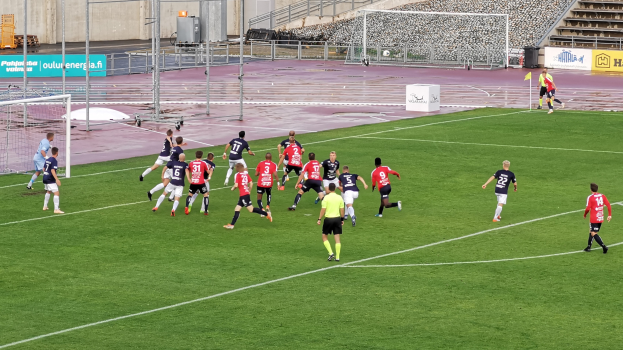 Eine Gruppe von Menschen, die Fußball auf einem Feld mit Zuschauern im Hintergrund eines Stadions spielen
